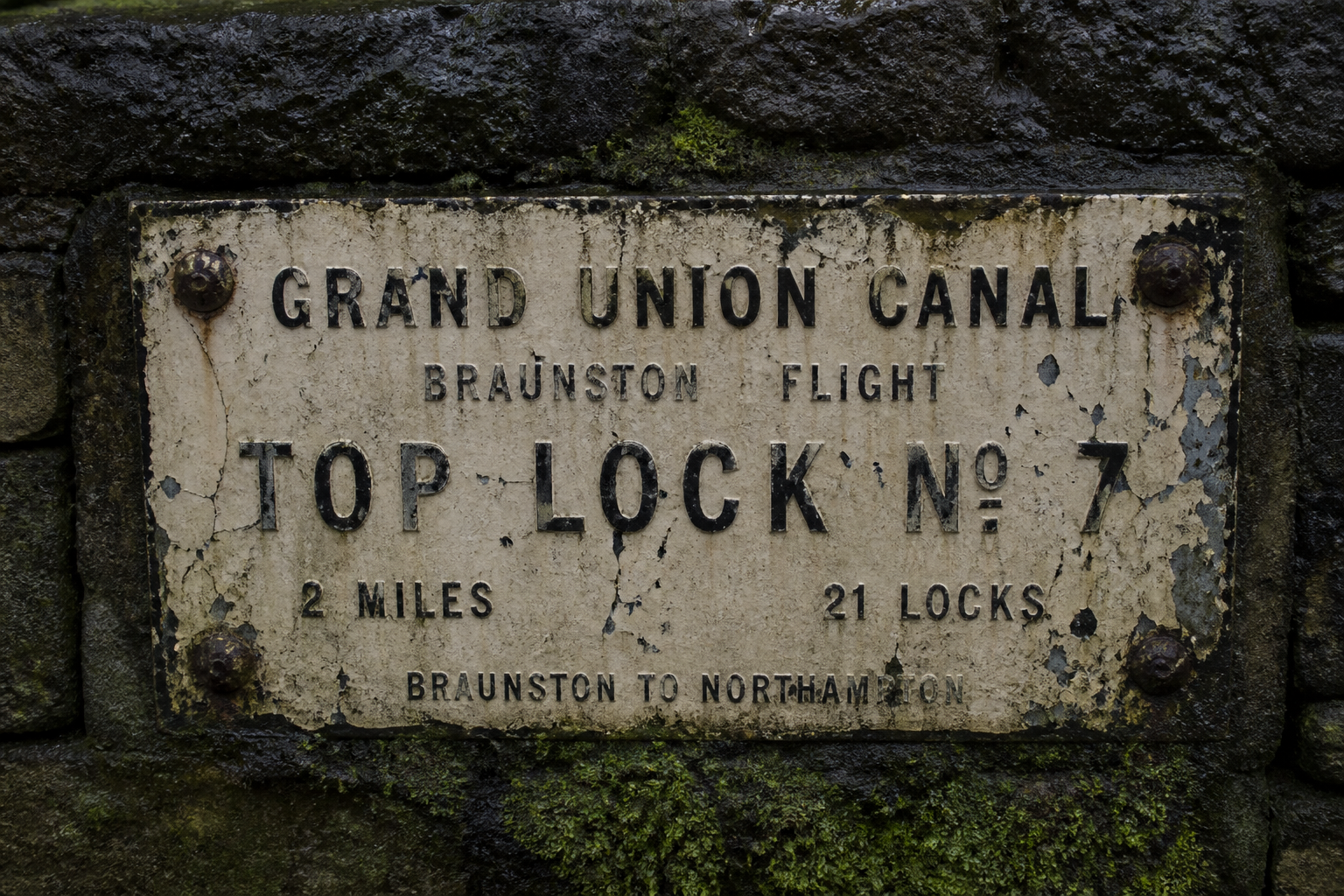 Weathered towpath sign on damp stone with rusted bolts